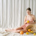 A peaceful woman in a pink dress holds a lemon, surrounded by citrus fruits, creating a refreshing mood.
