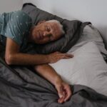 Elderly man resting comfortably in bed, serene indoor atmosphere.
