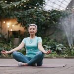 Elderly woman meditating in serene botanical garden setting, focused on wellness and mindfulness.