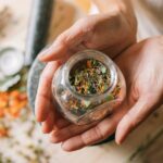 Close-up of hands holding a glass jar filled with colorful dried herbs.