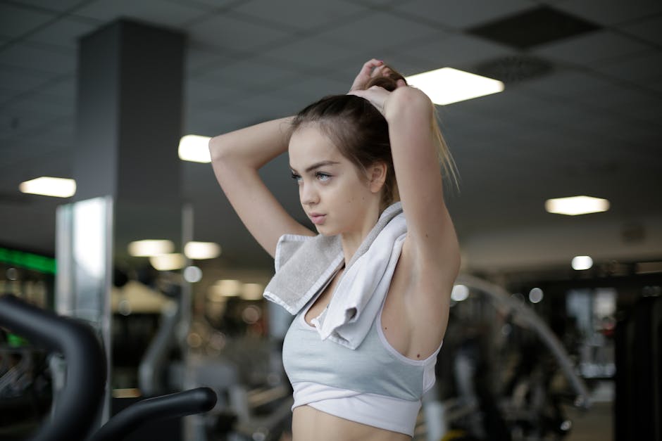 Woman adjusting ponytail in gym, ready to start her fitness routine. Determined and focused.
