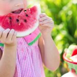 Young girl eating a juicy watermelon slice in a sunny outdoor setting, symbolizing summer refreshment.