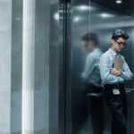 Young man in an elevator holding papers, deep in thought.