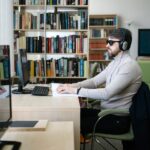 A blind man uses a computer with headphones in a library, highlighting technology's role in accessibility.